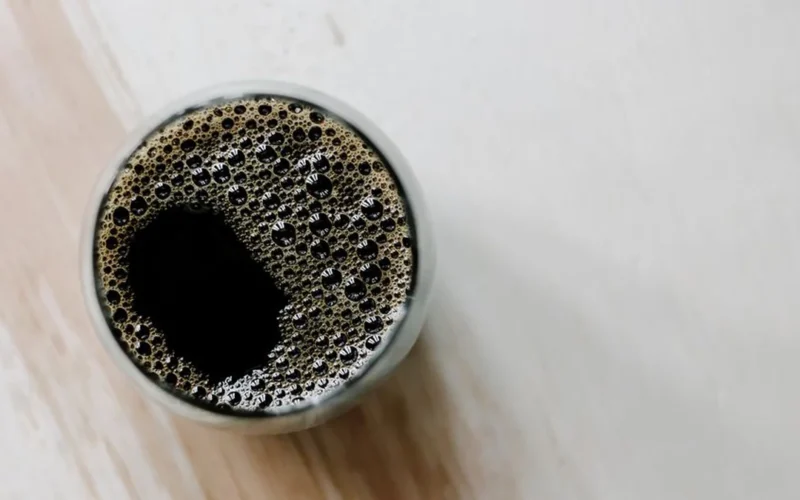 Steam rising from black coffee in a ceramic mug next to an espresso machine.