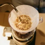 A professional barista performing a precision pour-over technique during a specialty coffee competition.