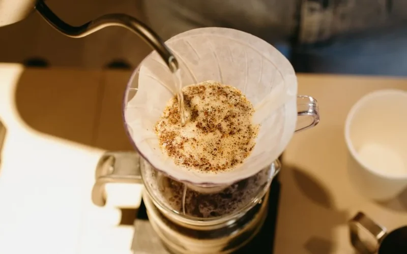 A professional barista performing a precision pour-over technique during a specialty coffee competition.