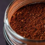 Close-up of instant coffee granules and green coffee beans on a wooden table.
