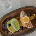 Close up of a seafood dish and a glass of white wine on a dining table.