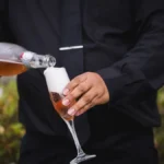 A sparkling wine flute beside an amber digestif in a crystal glass on marble.