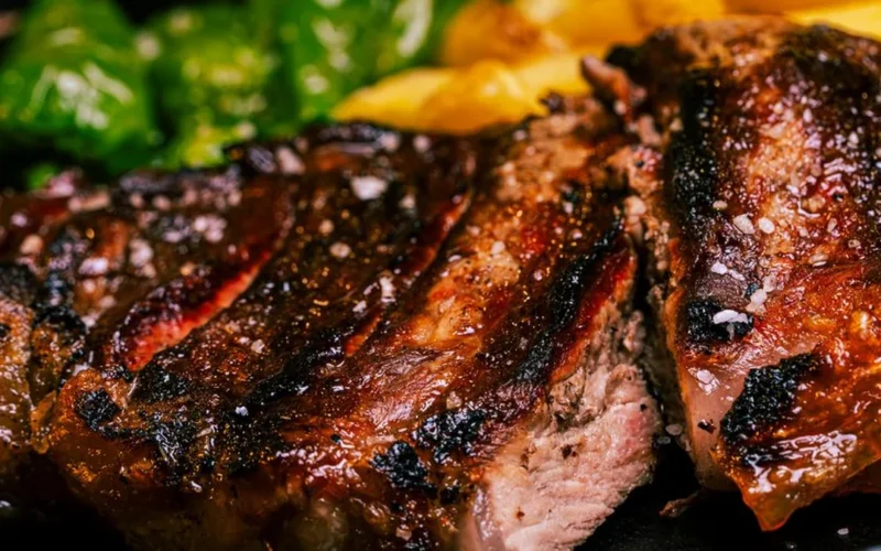 Sliced juicy ribeye steak served with a glass of red wine on a dark table.