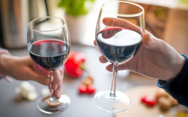 Three glasses containing different varieties of light-bodied red wine on a wooden surface.