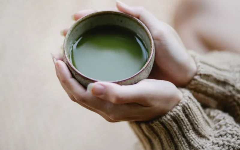 A bowl of whisked Uji matcha served alongside mochi and matcha cookies on a wooden surface.
