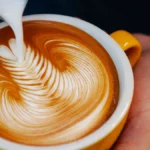 Close up of a barista pouring milk into an espresso cup to create latte art.