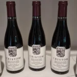 Three small half-bottles of Pinot Noir and wine glasses on a dark stone table.
