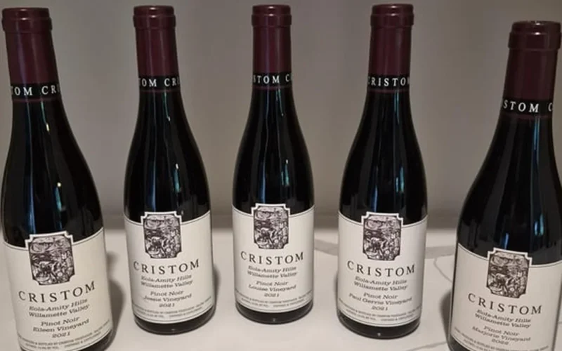 Three small half-bottles of Pinot Noir and wine glasses on a dark stone table.