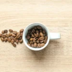 Dark caffeine-free coffee in a cup surrounded by date seeds and olive pits on wood.