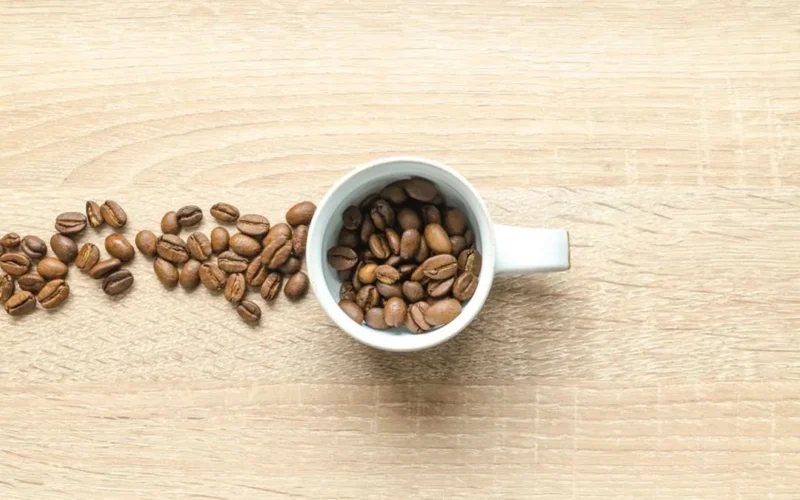 Dark caffeine-free coffee in a cup surrounded by date seeds and olive pits on wood.