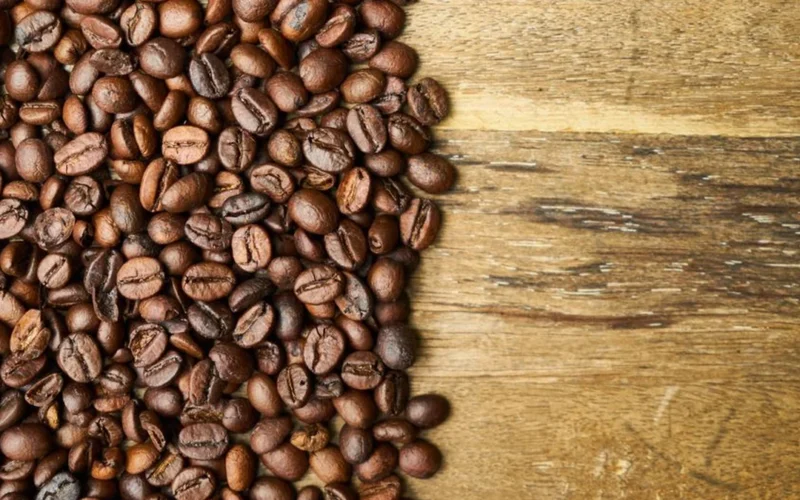 A variety of different specialty coffee bean types scattered on a dark textured surface.