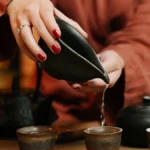An aged reddish Zhuni Yixing teapot and a cup of amber wulong tea on wood.