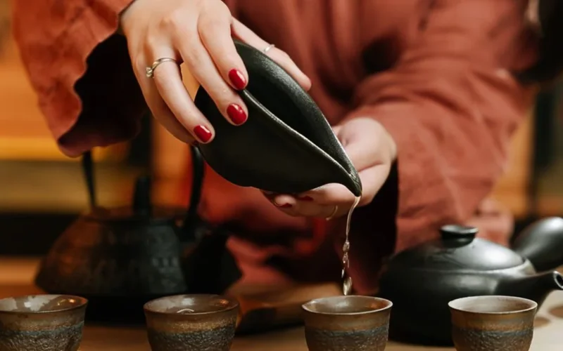 An aged reddish Zhuni Yixing teapot and a cup of amber wulong tea on wood.