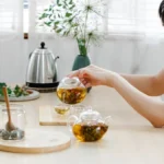 Amber colored oolong tea in a glass teapot beside loose tea leaves.