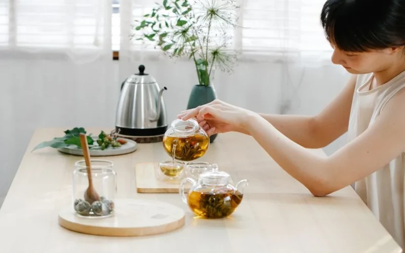 Amber colored oolong tea in a glass teapot beside loose tea leaves.