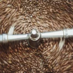 Roasted coffee beans spinning inside a professional stainless steel commercial drum roaster.