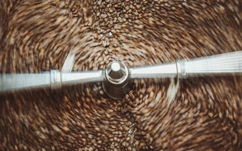 Roasted coffee beans spinning inside a professional stainless steel commercial drum roaster.