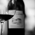 A bottle of Cornas Syrah and a glass set against terraced Northern Rhône vineyards.