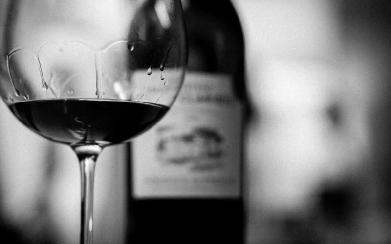 A bottle of Cornas Syrah and a glass set against terraced Northern Rhône vineyards.