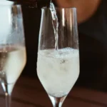 Pale white wine being poured into a glass overlooking an Okanagan Valley vineyard.