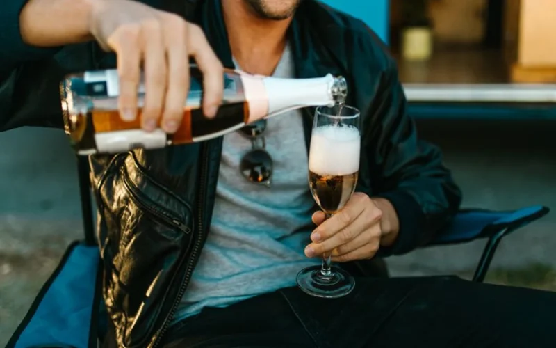An old bottle of champagne and a glass of amber colored liquid on wood.