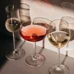 Two glasses of golden Chardonnay wine on a dark table with fresh peach slices.