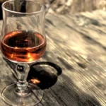 A close-up shot of red Burgundy wine poured into a crystal glass on a dark wooden surface.