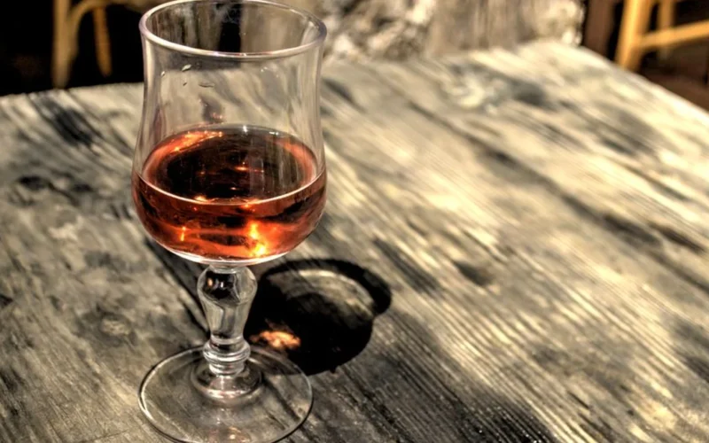 A close-up shot of red Burgundy wine poured into a crystal glass on a dark wooden surface.
