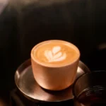 A creamy brown hojicha latte in a ceramic mug on a wooden coffee shop table.