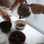 White milk being poured into a glass cup of dark black tea.