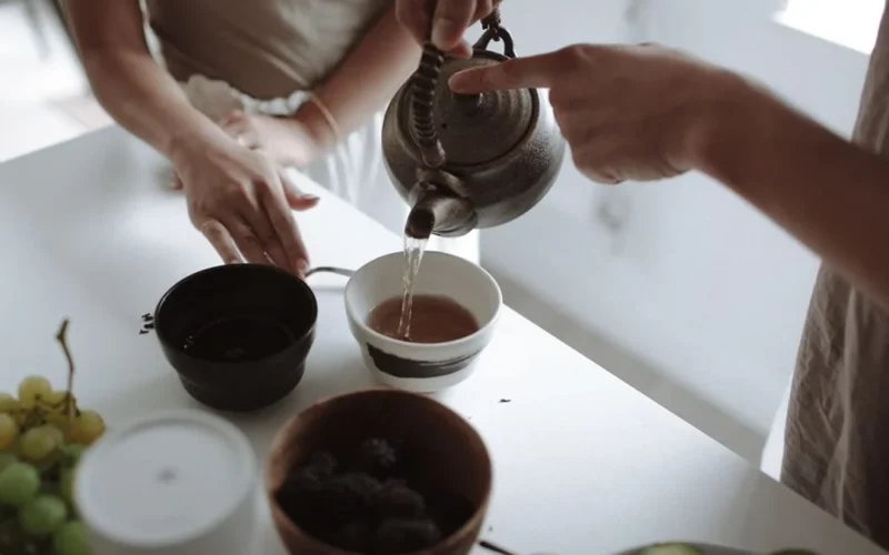 White milk being poured into a glass cup of dark black tea.