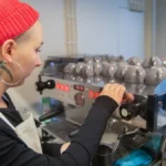 A female coffee professional managing operations in a bright specialty coffee shop environment.