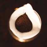 Traditional South Indian filter coffee served in a brass tumbler with spices on a wooden surface.