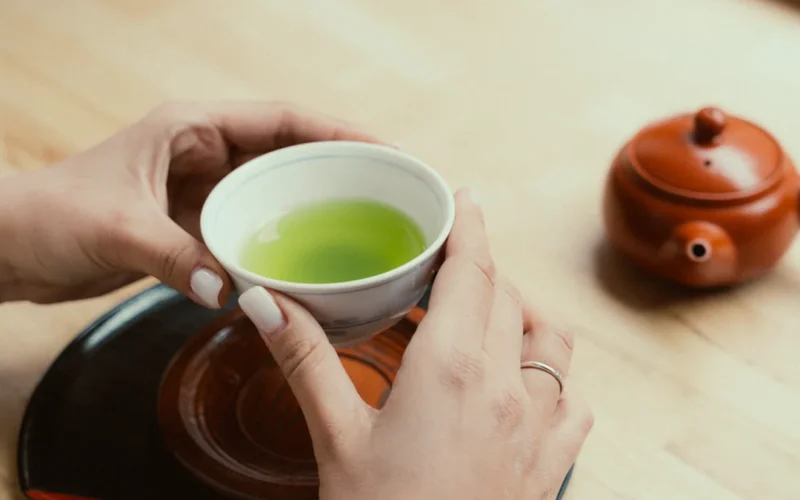 Bright green matcha powder in a bowl beside traditional dried sencha tea leaves.