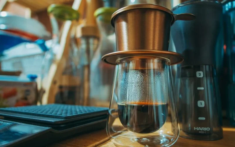 Close up of coffee beans, a burr grinder, and a glass carafe on a kitchen counter.