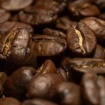 Macro shot of dark roasted coffee beans next to white caffeine crystals on slate.