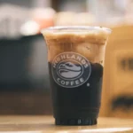 Iced coffee with coconut milk foam served on a textured stone surface.