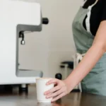 Barista handing a coffee cup and retail bean bag to a customer at a cafe counter.