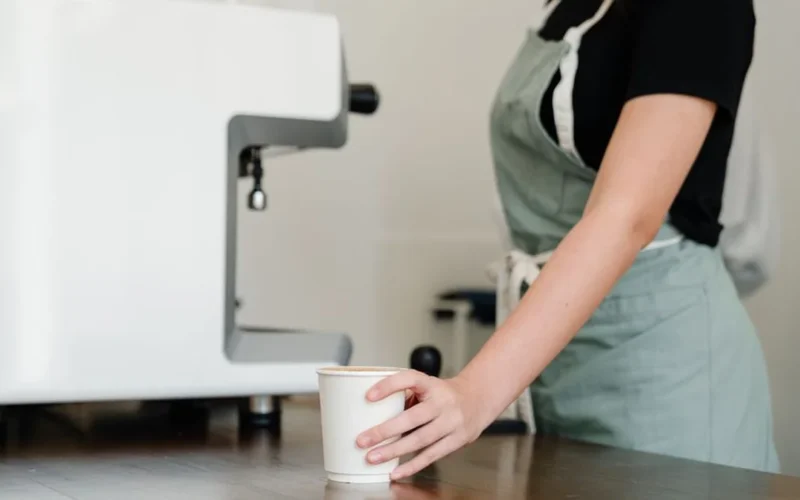 Barista handing a coffee cup and retail bean bag to a customer at a cafe counter.