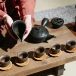 Ceramic gaiwan and tea cup with loose leaf oolong tea on wooden surface.