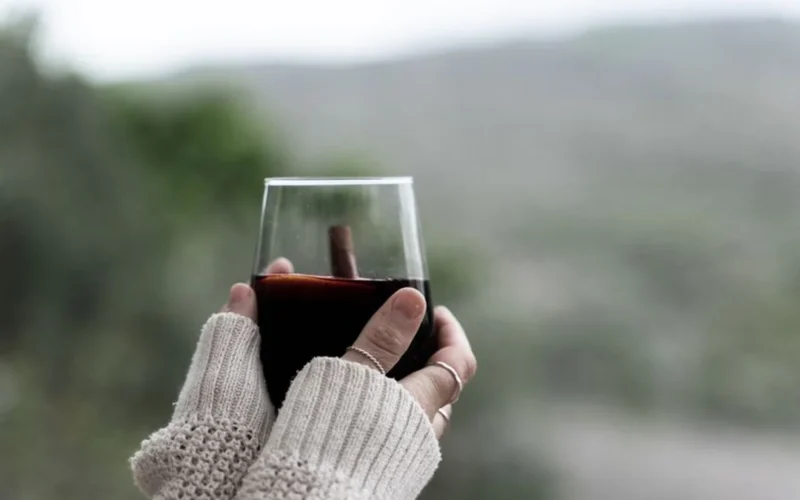 Person holding a glass of light red wine in a sunny California vineyard.