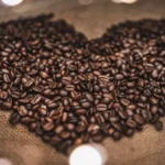 Raw green coffee beans overflowing from a textured jute burlap sack on a wooden table.