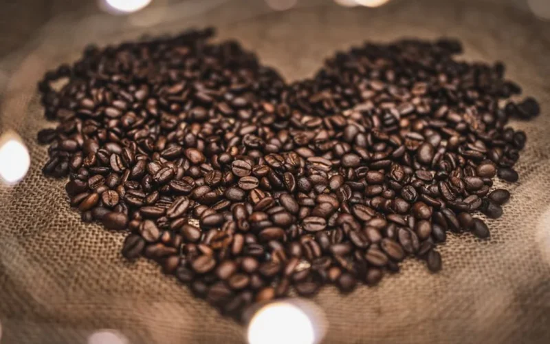 Raw green coffee beans overflowing from a textured jute burlap sack on a wooden table.
