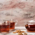 A handmade Yixing clay teapot beside dried Jin Jun Mei tea leaves on stone.