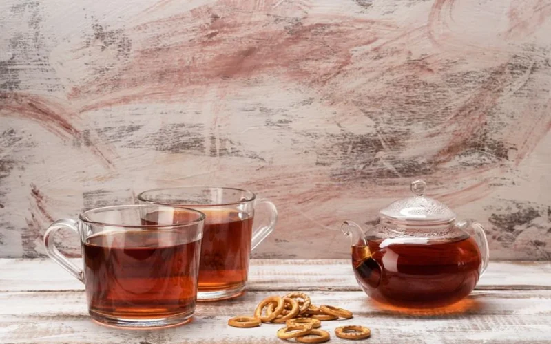 A handmade Yixing clay teapot beside dried Jin Jun Mei tea leaves on stone.