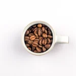 Whole roasted coffee beans next to a professional espresso machine on a kitchen counter.