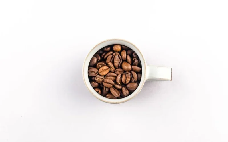 Whole roasted coffee beans next to a professional espresso machine on a kitchen counter.
