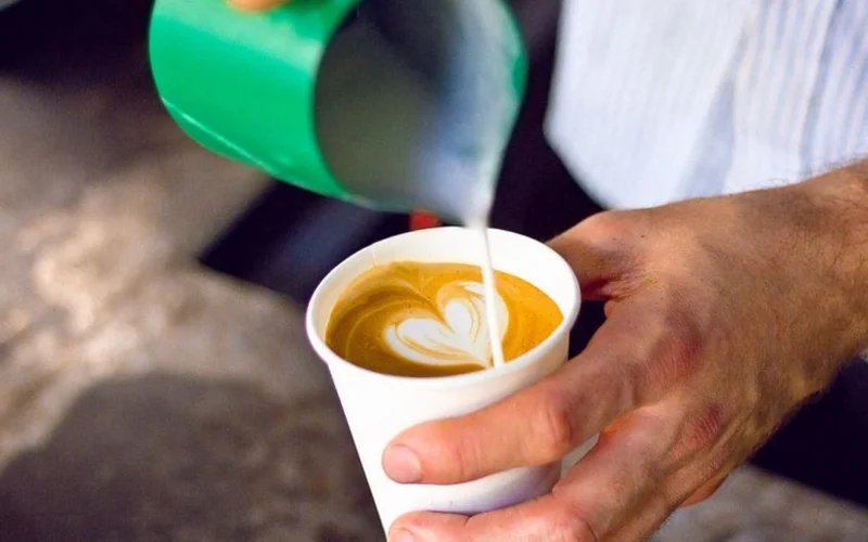 Close up of a barista pouring milk to create latte art in a ceramic cup.