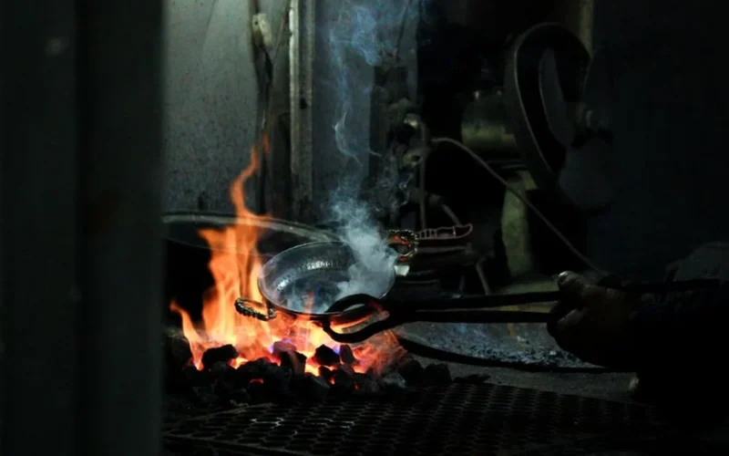 An elderly craftsman pan-firing green tea leaves in a traditional wok at an expo.