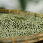 Close-up of raw green arabica coffee beans overflowing from a burlap sack on wood.